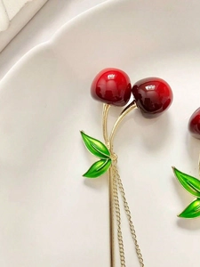 Detail of red cherry hair pin with green leaves and gold chain tassel on white tray