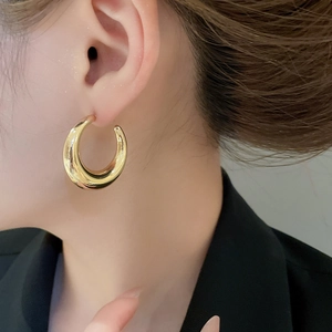 Close-up of a large polished gold C-shaped hoop earring worn by a model