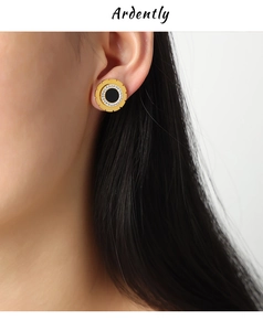 Close-up of gold-plated gear earrings with inset crystals and black enamel inlay