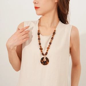 Détail de perles en bois et pendentif en résine ambre sur un collier long Maillard