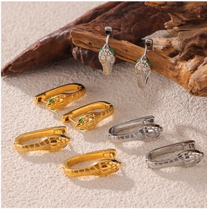 Detail of gold and silver snake earrings with gemstone eyes on a textured wooden stand