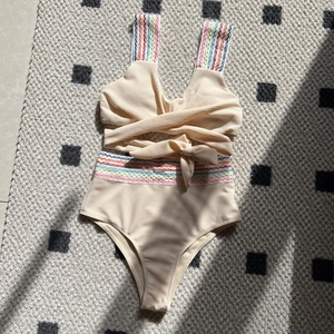 Flat lay of high-waisted beige bikini set with colorful rainbow wave embroidery details