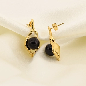 Detailed shot of gold irregular geometric earrings with black pearls on silk background