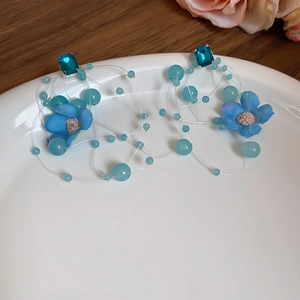 Detail of blue floral earrings with hanging crystals and pearls on white ceramic plate