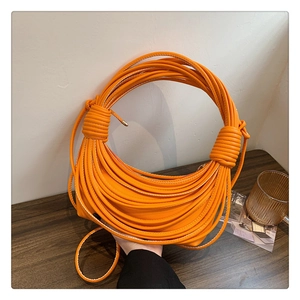 Detail of the bright orange knotted handle design and soft leather texture on this shoulder bag
