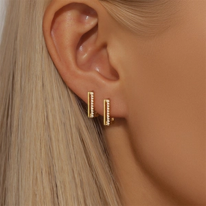 Close-up of gold rectangular hoop earrings with paved cubic zirconia worn by a model