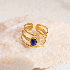 Detailed close-up of a layered gold ring with an oval blue natural stone on a textured rock