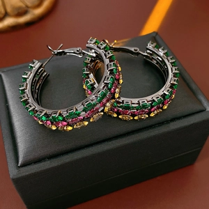 Macro shot of dark metal hoop earrings with emerald and ruby colored crystals on a box