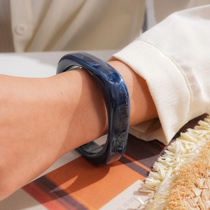 Detailed shot of a navy blue marbled resin square bangle worn on a model's wrist