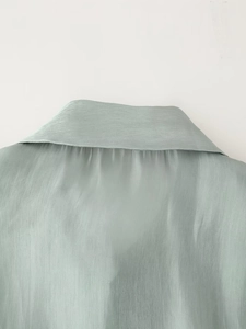 Close-up of the light green glossy shirt neckline with a detailed bow tie and silky texture