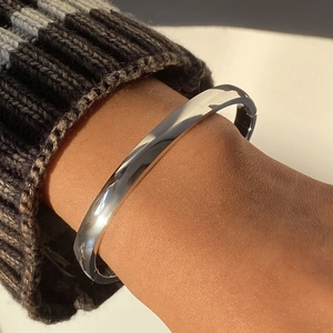 Close-up of a polished stainless steel minimalist bangle worn over a knit sweater sleeve