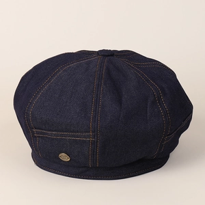 Detail of dark blue denim newsboy cap with yellow contrast stitching and metal badge
