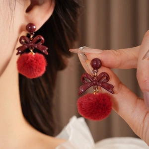Detailed view of red bow earrings with plush pom poms worn on ear for style and size