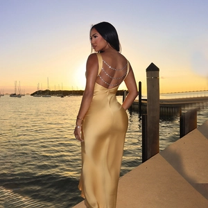 Elegant gold satin backless maxi dress with triple-layer rhinestone chains at sunset pier