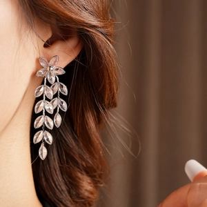 Detail of silver drop earrings featuring floral tassels and clear zircon crystals on a model