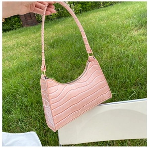 Pink faux crocodile leather shoulder bag held against a natural green grass background