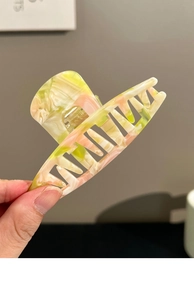 Macro detail of acrylic hair claw clip showing yellow-green and pink tortoiseshell pattern