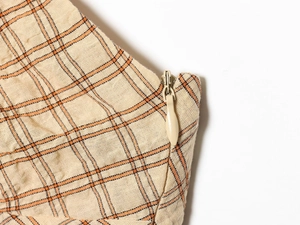 Detail shot of invisible zipper closure on beige plaid fabric with orange and black lines