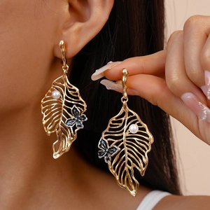 Detail of gold monstera leaf earrings with pearl accents and black metal butterflies