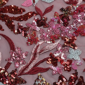 Detailed macro view of delicate sequins and floral embroidery on burgundy mesh fabric