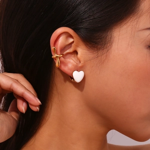 Detailed view of 18K gold-plated cross ear cuff and white heart stud on a model