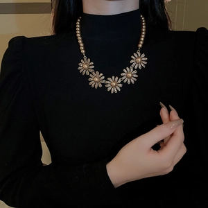 Close-up of elegant gold pearl necklace with diamond daisy flowers worn by a model