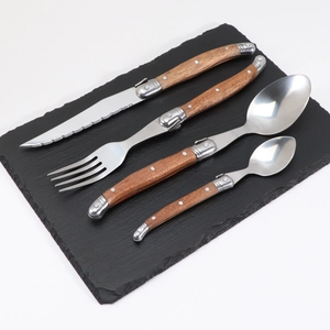 Laguiole style stainless steel cutlery set with wood handles on a dark slate board