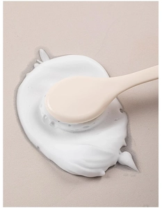 Close-up of beige facial cleansing brush applying rich white foam on a smooth surface