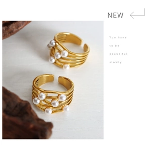 Detail of gold layered wave rings with white pearls on a textured white surface