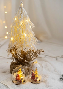 Close-up of a glowing flocked Christmas tree and glass Santa LED ornaments on fake snow