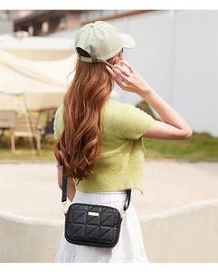 Outdoor shot of a black quilted crossbody camera bag with triangle embroidery detail