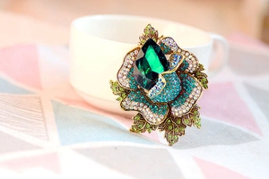 Macro shot of luxury flower brooch with emerald crystal and blue rhinestones on a white cup