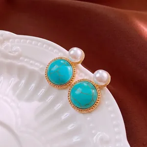 Vintage gold-rimmed turquoise and pearl earrings displayed on elegant white ceramic dish