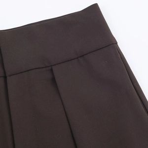Vue macro d'un pantalon marron foncé montrant les plis de taille et la texture sergé
