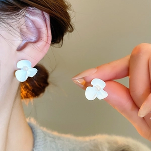 Detailed close-up of a white matte flower earring with a pearl center on a model's ear