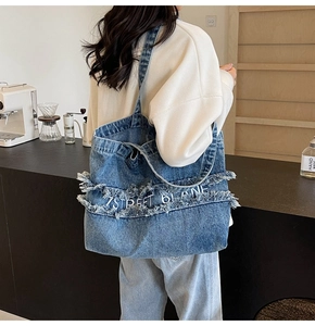 Détail du grand sac cabas en denim bleu avec bords effilochés et broderie blanche