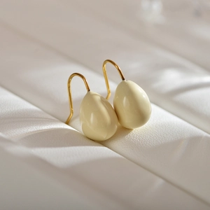 Close-up of cream teardrop earrings with gold hooks on a white leather texture background