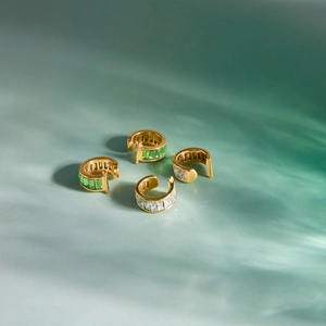 Gros plan de quatre boucles d'oreilles C dorées 18k avec zircons carrés verts et blancs