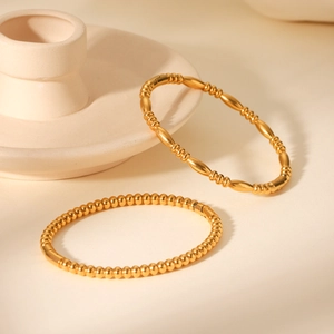 Close-up of polished 18K gold stainless steel beaded bracelets on beige ceramic base