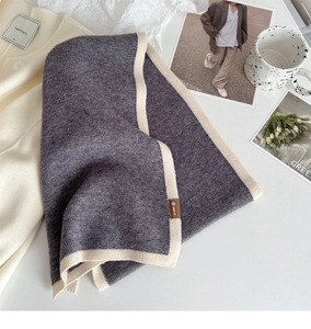 Detailed close-up of dark grey knit scarf with beige border and small leather label