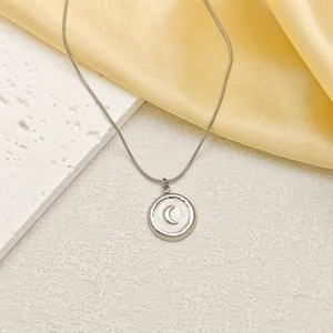 Détail macro du pendentif lune en argent sur pierre blanche et fond de satin jaune