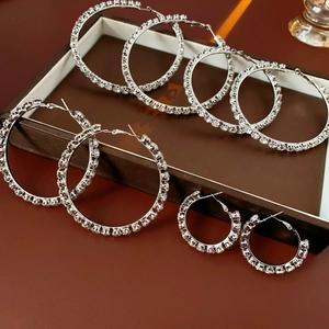 Detailed view of silver diamond hoop earrings in three sizes on a brown tray