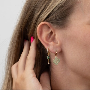 Close-up of gold earrings with green zircon cactus and emerald stone pendants