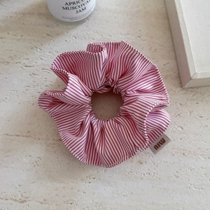Detail of red and white striped scrunchie with miu woven label on marble surface