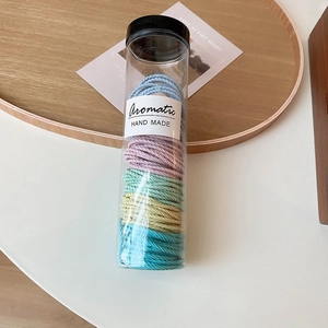 Rainbow elastic hair ties stored in a transparent cylinder on a minimalist wooden tray