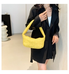 Yellow floral quilted hobo bag with wide shoulder strap worn by a model in a black coat
