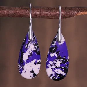Macro detail of teardrop earrings with purple marble texture hanging on a wooden branch