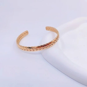 Macro shot of rose gold C-shaped wheat pattern bangle on a white minimalist stone base
