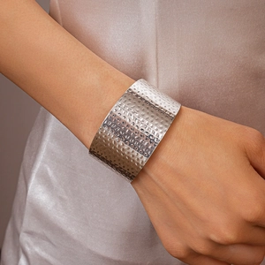 Detail of a wide hammered silver metal cuff bracelet featuring a unique textured finish
