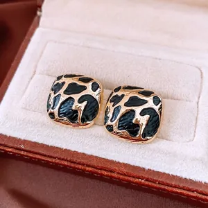 Square gold leopard print enamel stud earrings displayed on premium beige velvet
